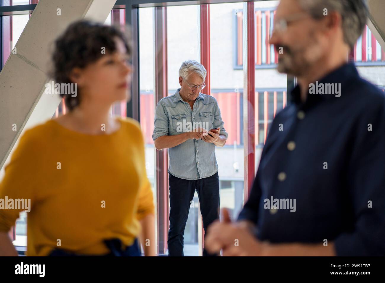 Geschäftsfrau spricht mit Geschäftsmann und Kollegen mit Smartphone im Hintergrund Stockfoto