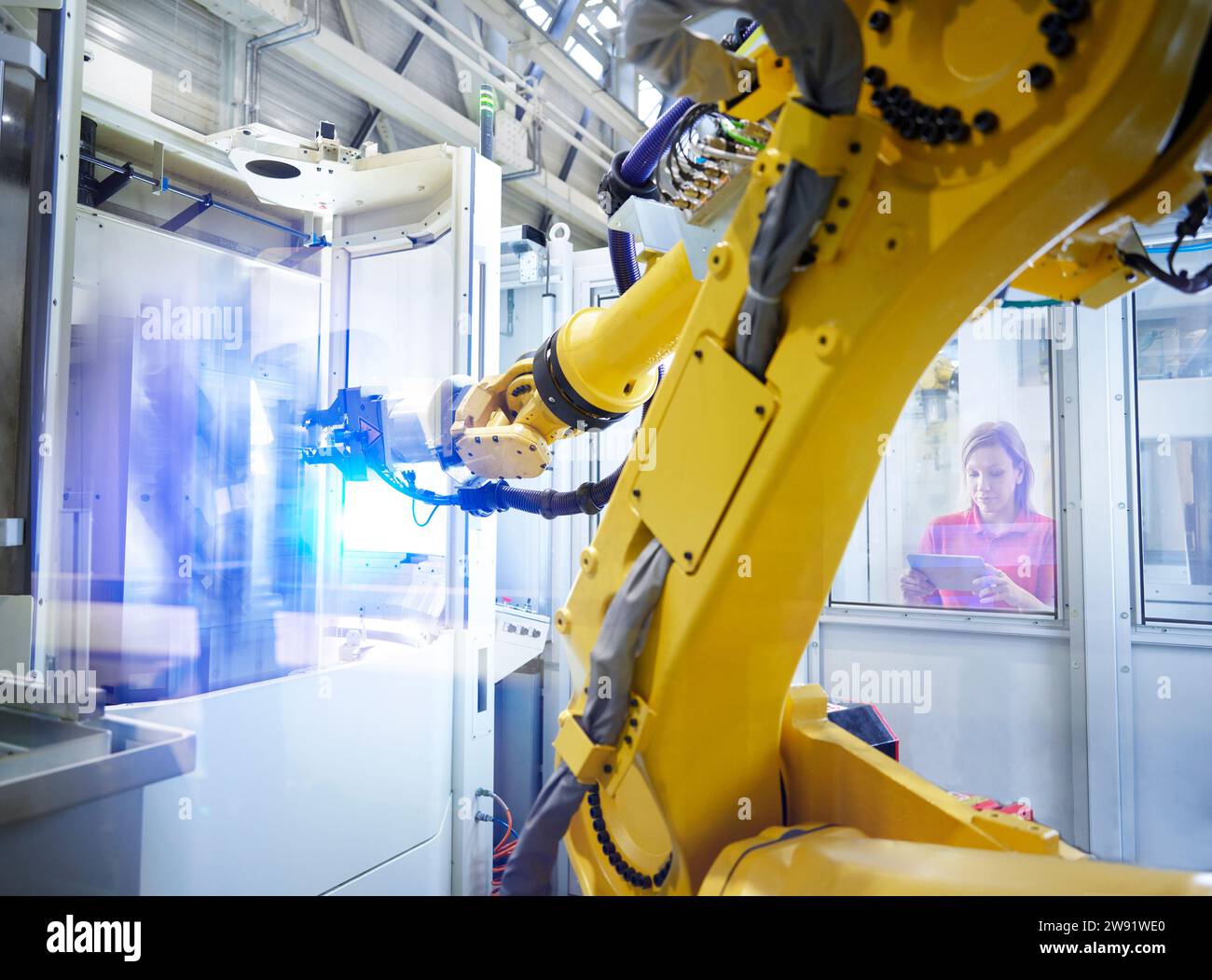 Techniker, der den gelben Roboterarm werkseitig über den Tablet-PC bedient Stockfoto