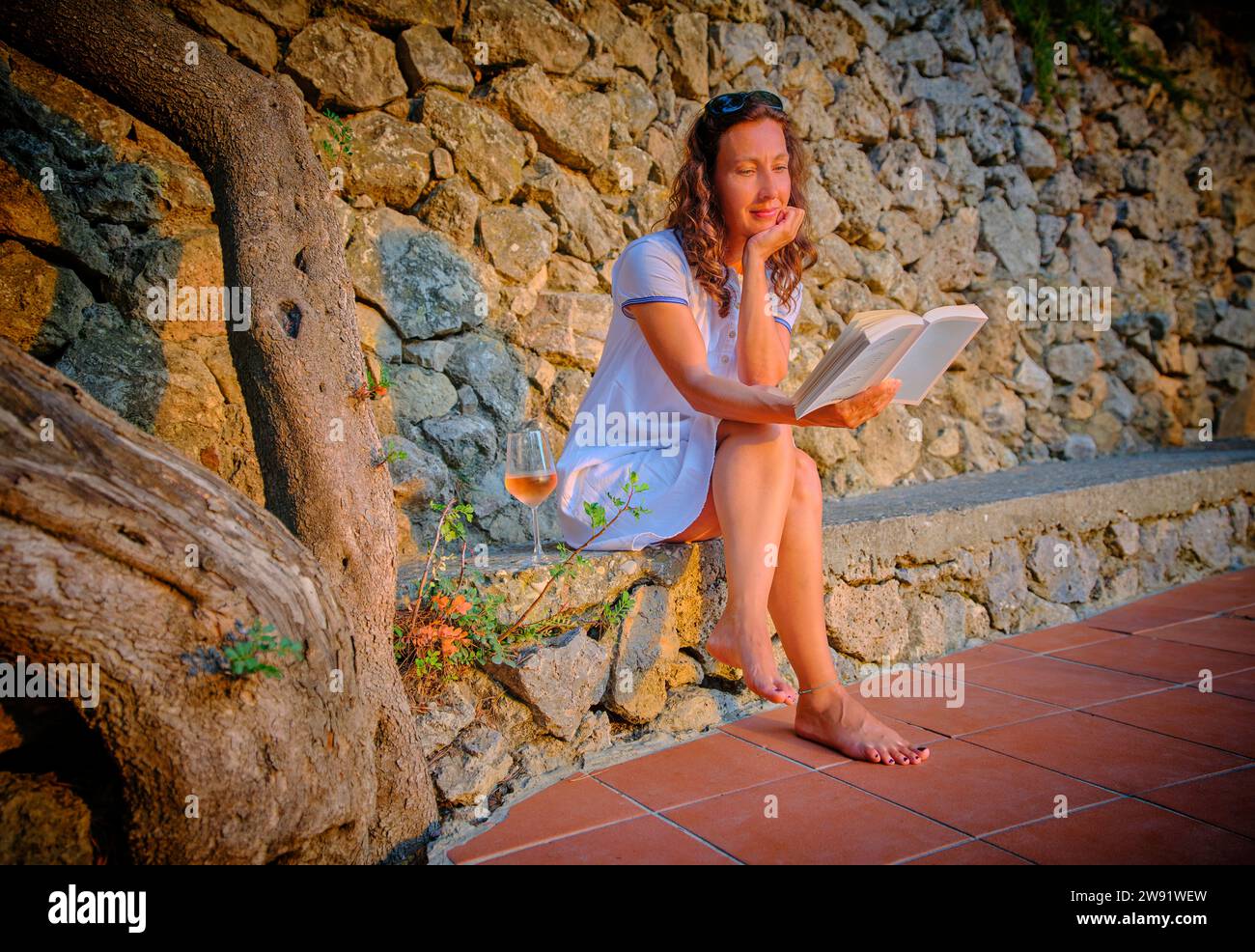 Frau liest Buch in der Nähe einer Steinmauer Stockfoto