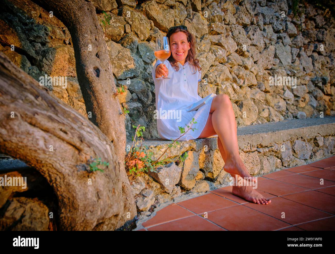 Lächelnde Frau genießt ein Glas Wein in der Nähe einer Steinmauer Stockfoto