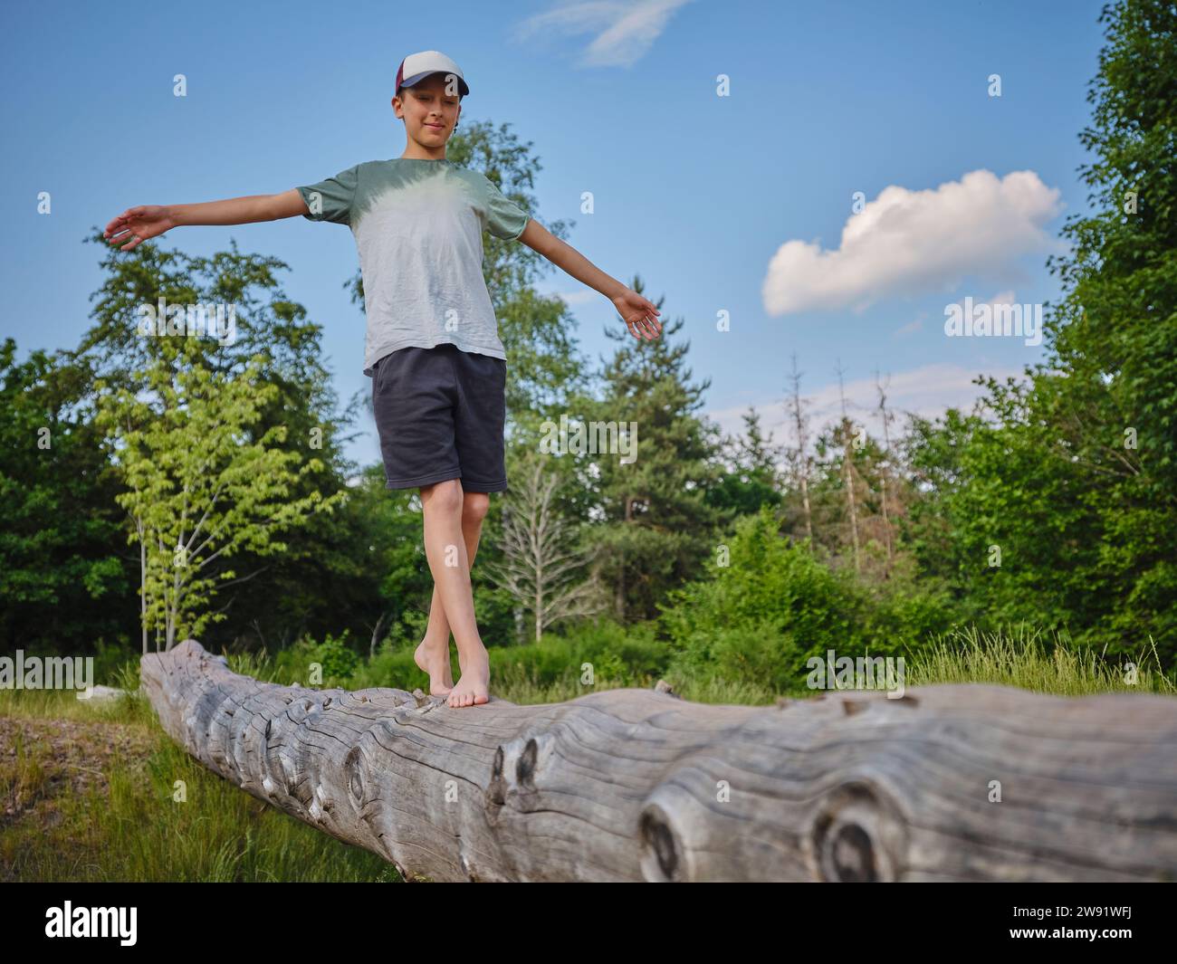 Junge mit ausgestreckten Armen balancieren und auf Baumstamm im Wald laufen Stockfoto