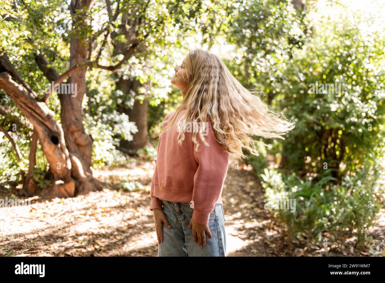 Lächelndes Mädchen mit langen blonden Haaren steht im Park Stockfoto