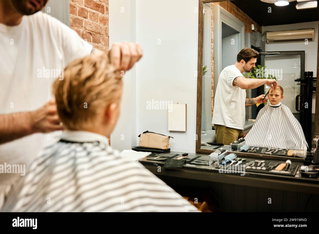 Friseur schneidet die Haare des Kunden vor dem Spiegel im Salon Stockfoto