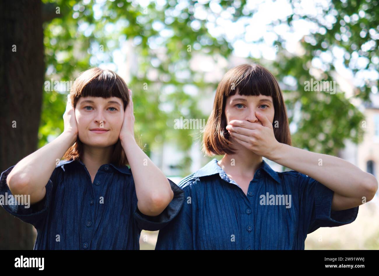 Zwillingsschwestern bedecken Mund und Ohren mit Händen vor dem Baum Stockfoto