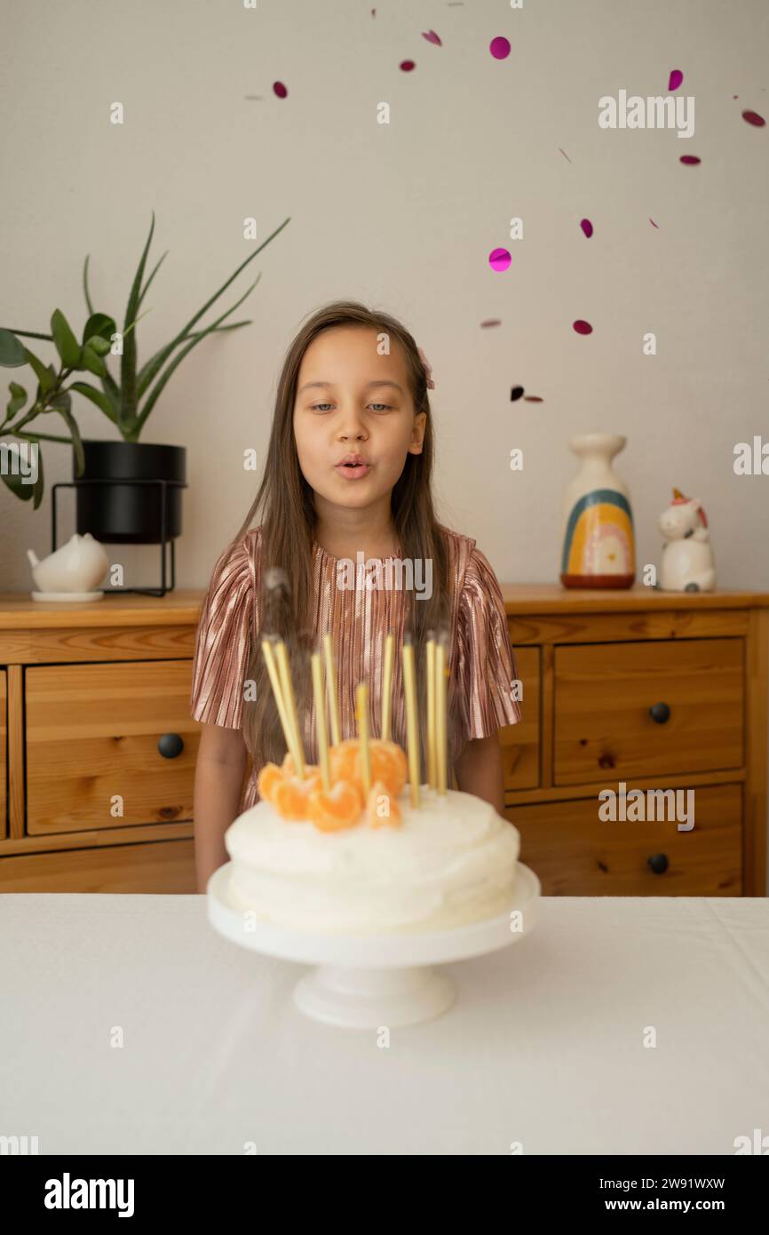 Glückliches Mädchen, das zu Hause Kerzen auf Geburtstagskuchen bläst Stockfoto