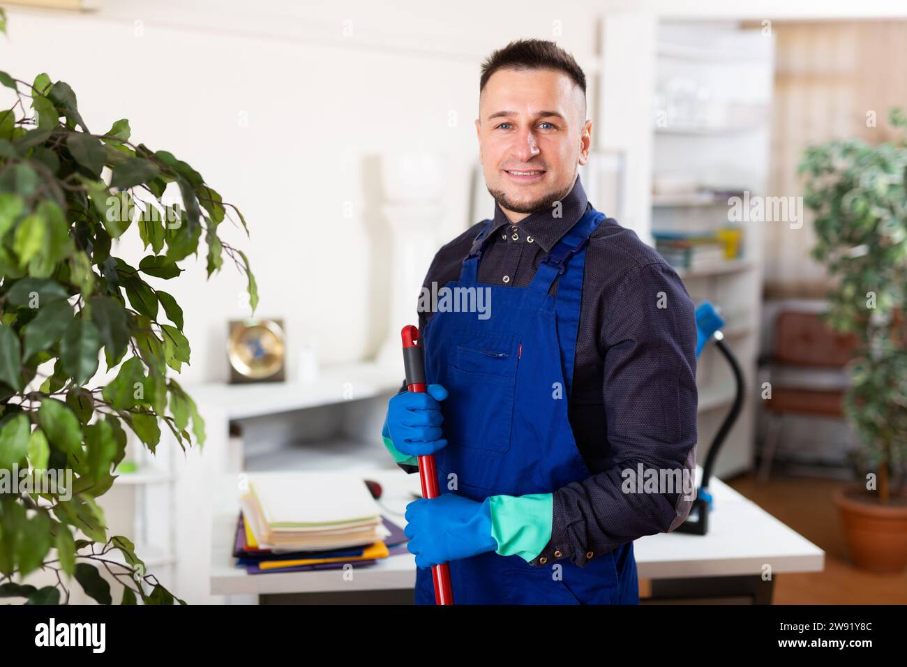 Männlicher professioneller Hausmeister, der im Büroinneren Staub staubt Stockfoto
