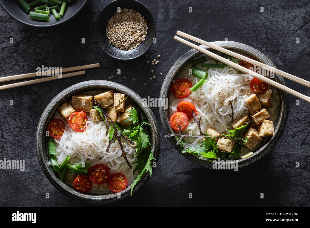 Schüsseln mit veganer Tom-Kha-Kai-Suppe mit Tofu, Tomaten, Salat, Reisnudeln, Sesamsamen und Zwiebeln Stockfoto