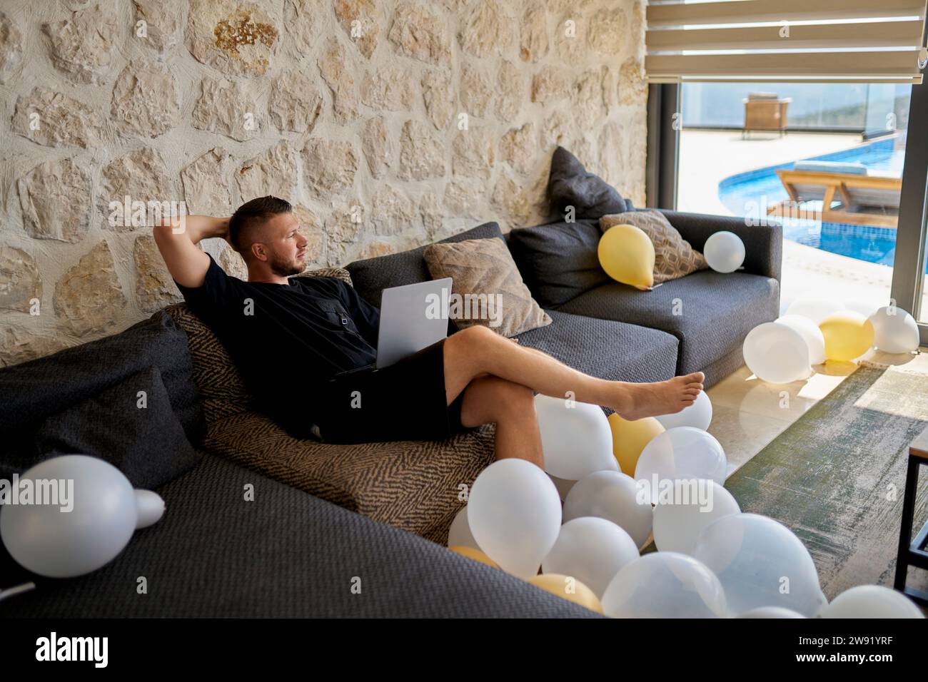 Freelancer mit Laptop, der in der Villa in Ballons auf dem Sofa sitzt Stockfoto