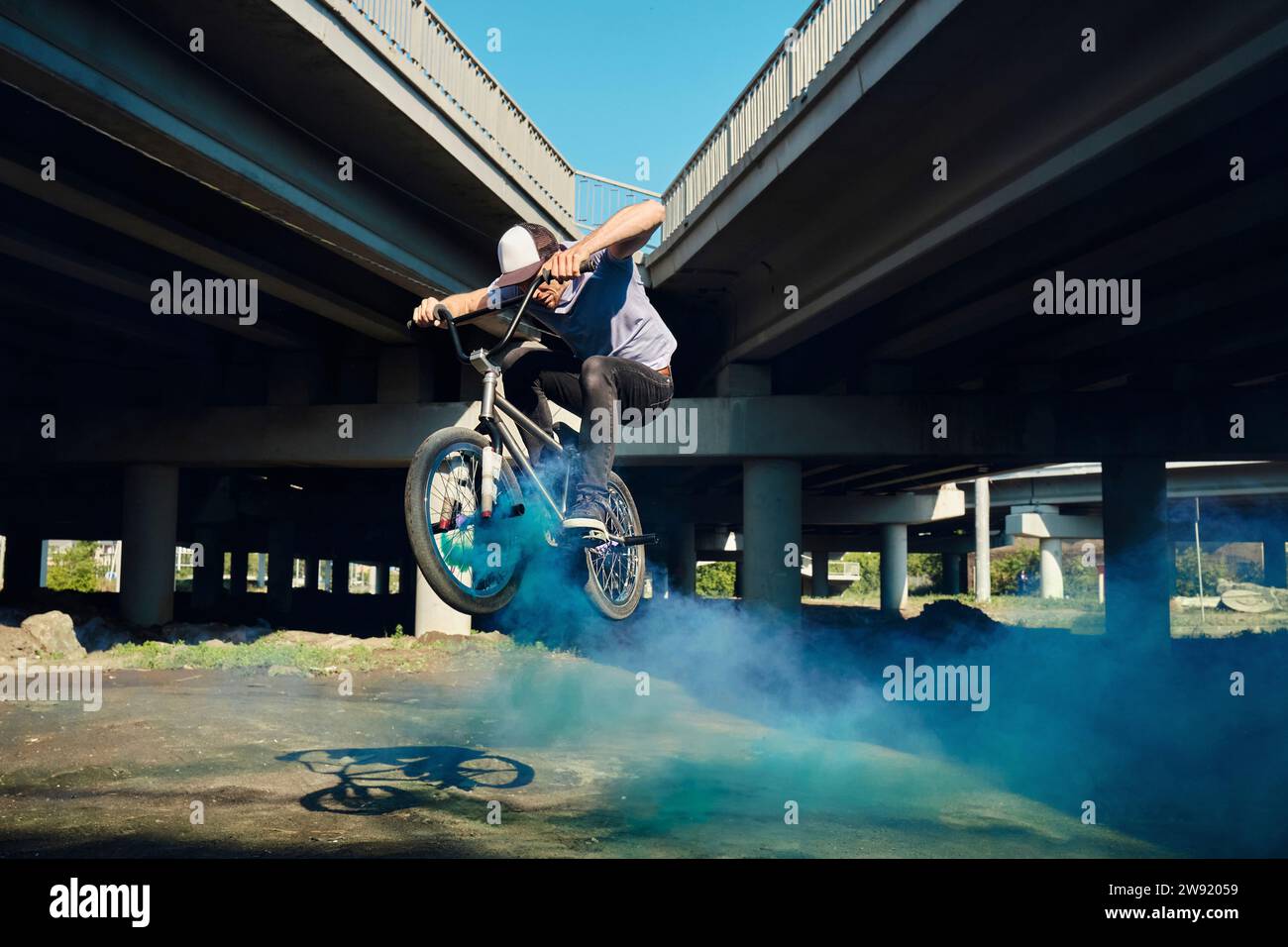 Mann, der mit BMX-Fahrrad springt und blauen Rauch in der Nähe der Brücke ausstrahlt Stockfoto