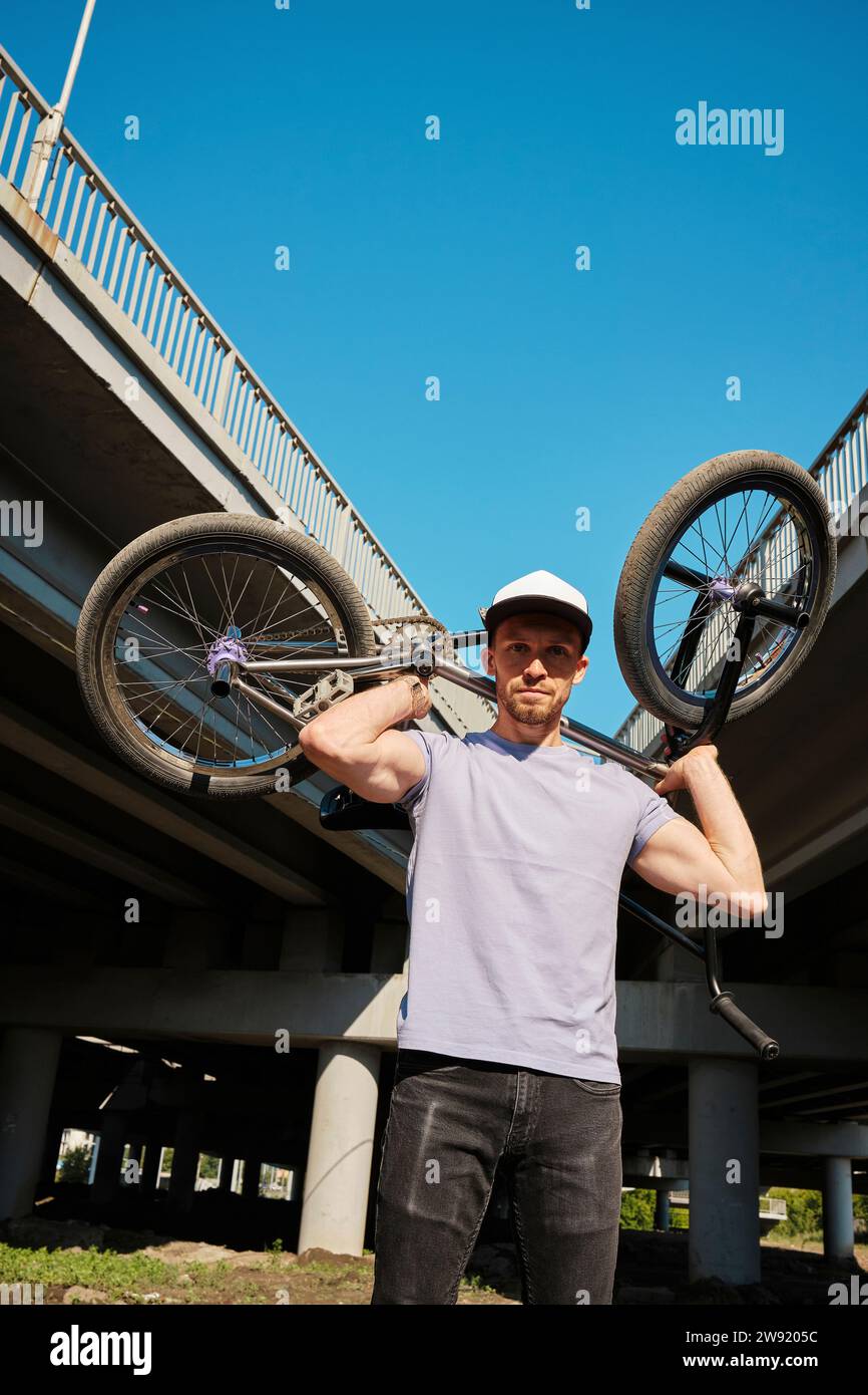 Mann, der BMX-Fahrrad über Schultern in der Nähe der Brücke trägt Stockfoto