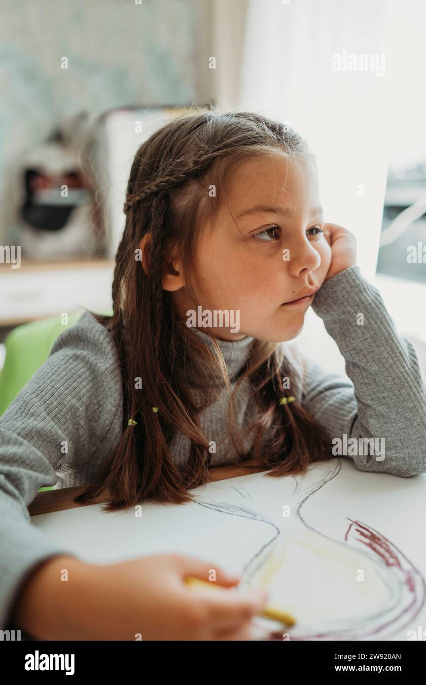 Ein nachdenkliches Mädchen sitzt mit Buntstift und Papier am Tisch Stockfoto