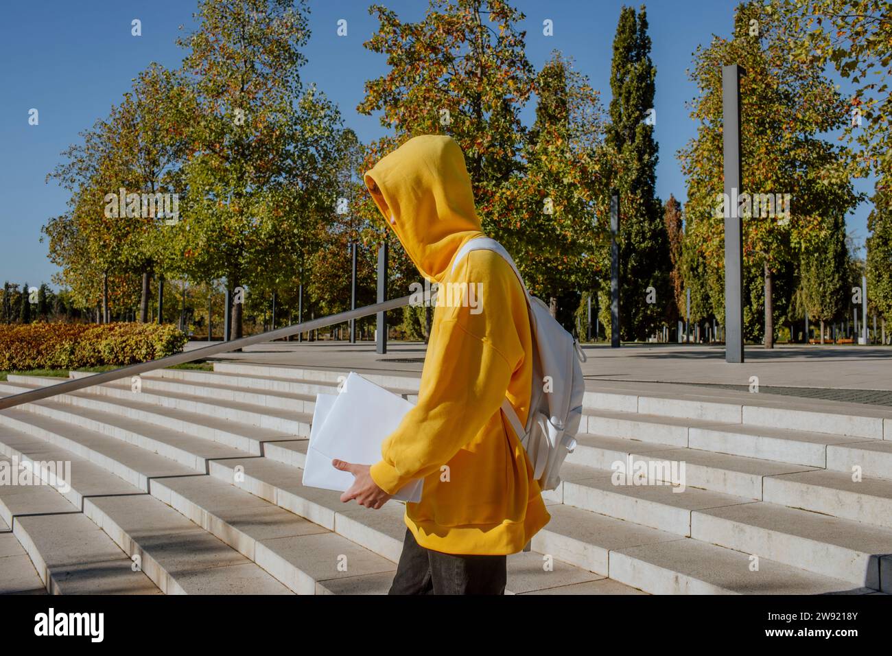 Der Schüler trägt ein gelbes Kapuzenhemd, hält Bücher und geht auf Stufen hinunter Stockfoto
