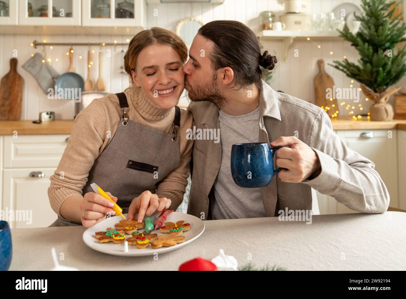 Mann küsst eine Frau, die Kekse am Tisch dekoriert Stockfoto