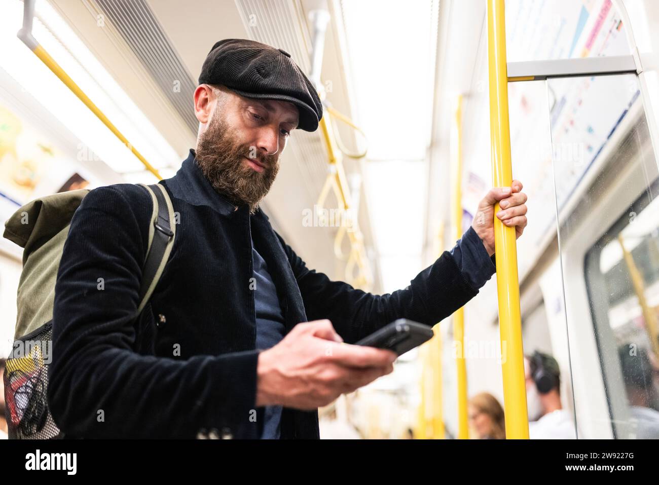 Mann, der die Stange hält und im Zug ein Smartphone benutzt Stockfoto