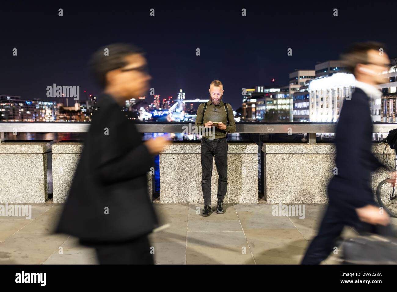 Mann, der sein Smartphone benutzt und nachts in der Stadt neben dem Geländer steht Stockfoto