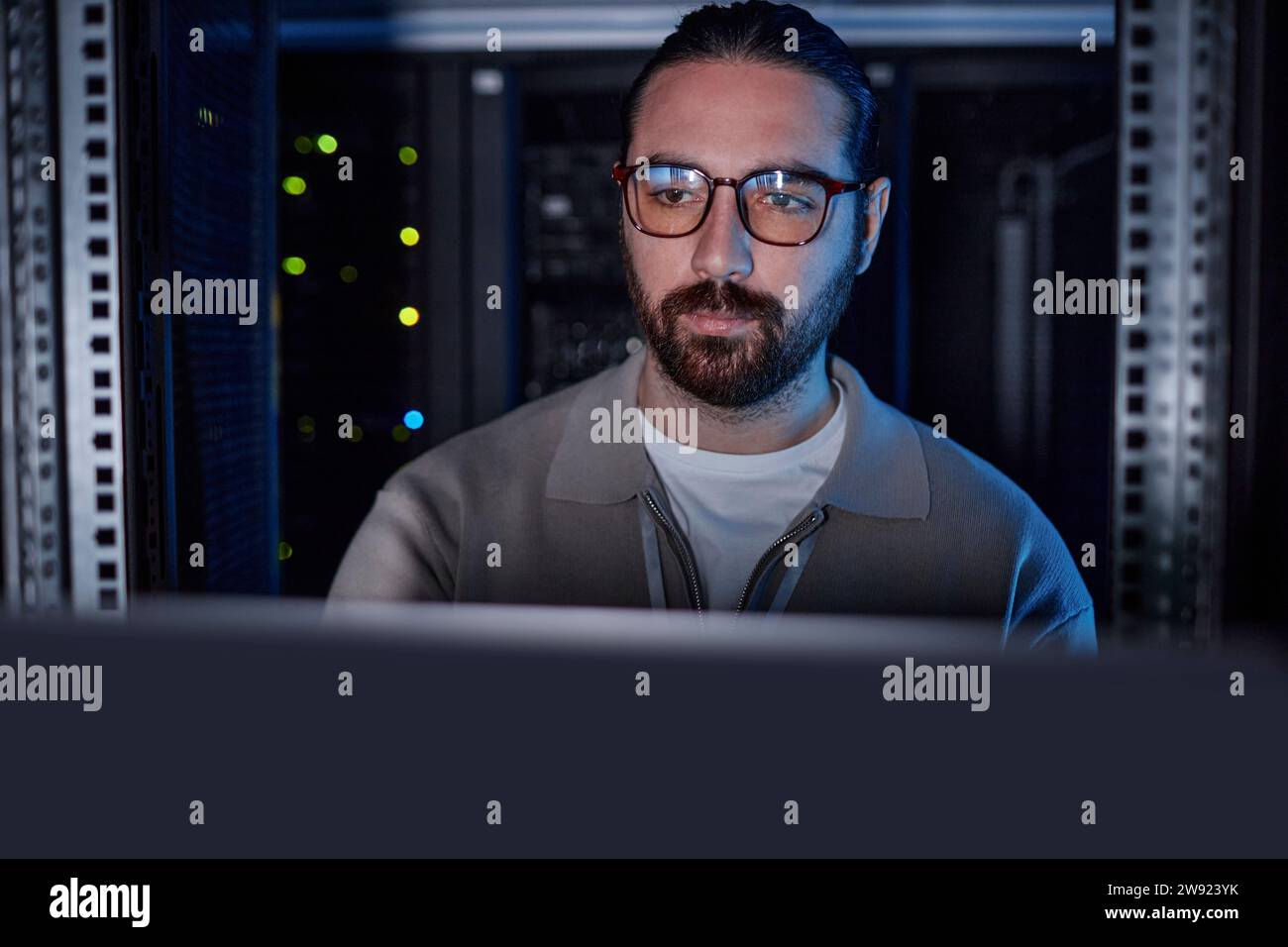 Junger Ingenieur, der eine Brille trägt und im Serverraum an einem Laptop arbeitet Stockfoto