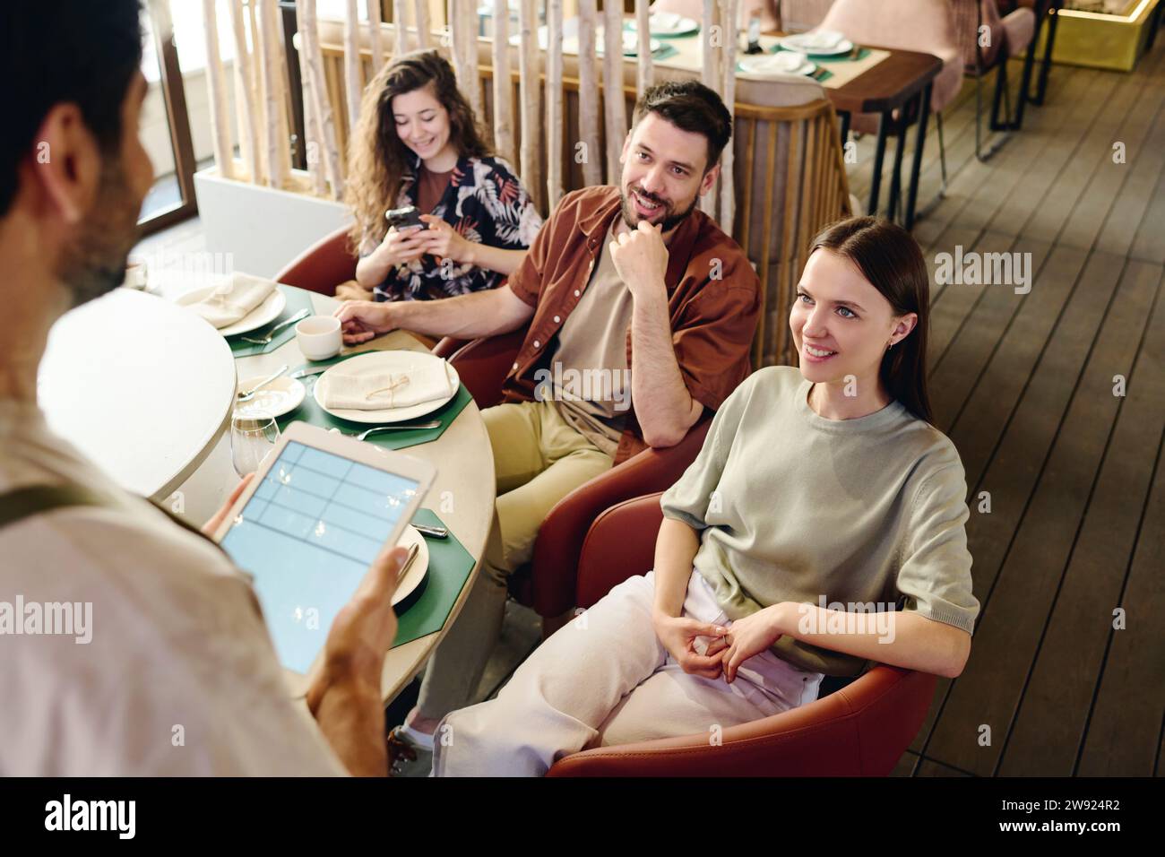 Glückliche Freunde, die dem Kellner mit Tablet-PC Essen bestellen Stockfoto