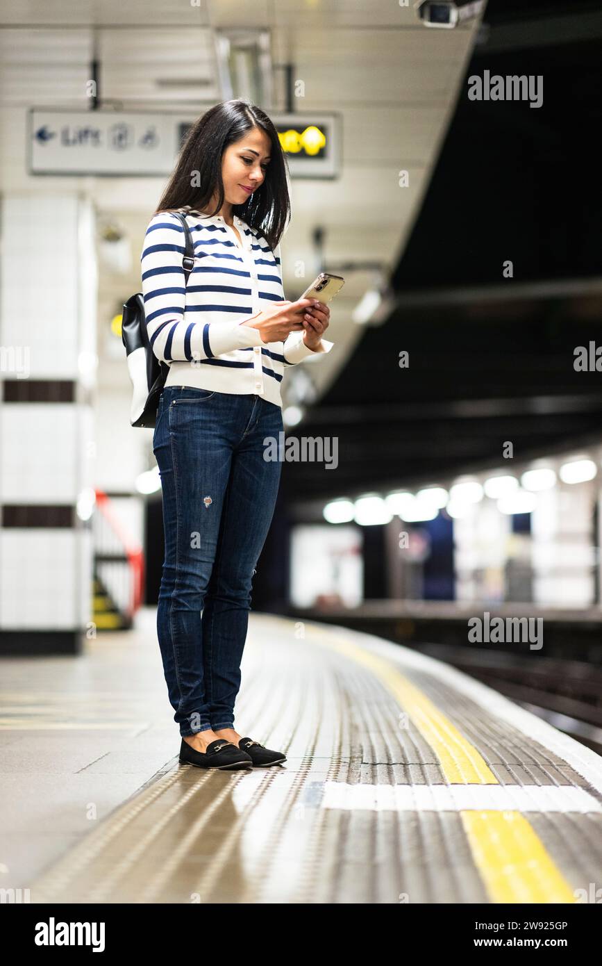 Frau, die das Handy auf dem Bahnsteig der U-Bahn benutzt Stockfoto