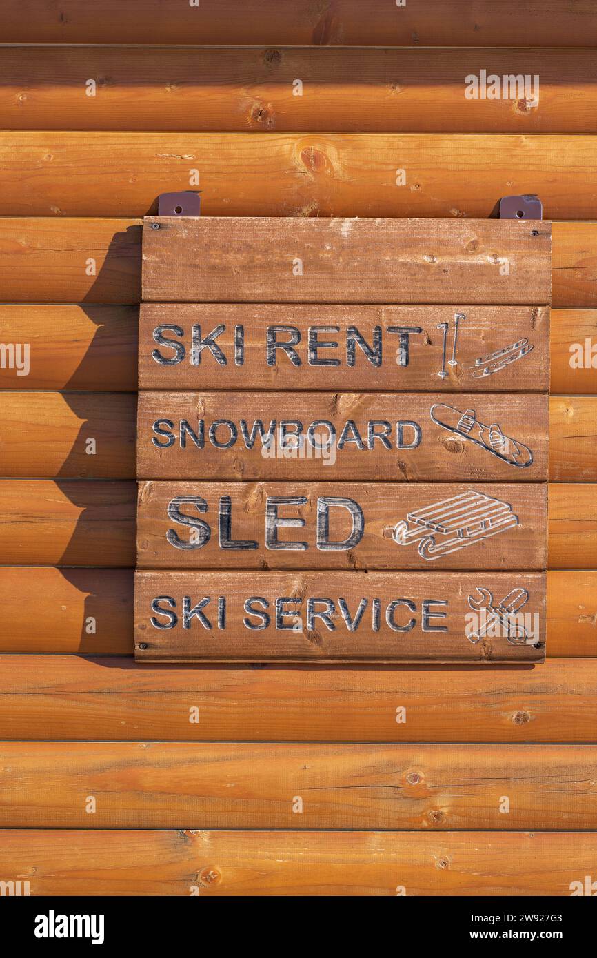 Informationstafel mit braunen Holzdielen. Service des Skizentrums. Skiverleih, Schlitten und Snowboard. Schwarze Buchstaben, Symbole. Wörter. Stockfoto