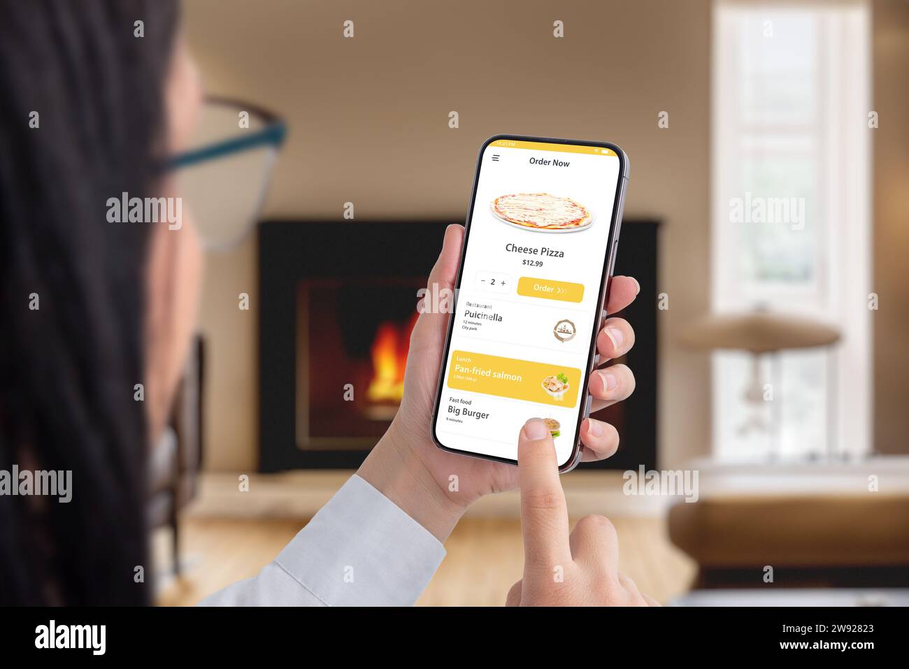 Frau bestellt online Pizza mit Smartphone-App in einem gemütlichen Zimmer am Kamin. Nahtloser Komfort für ein köstliches kulinarisches Erlebnis zu Hause Stockfoto