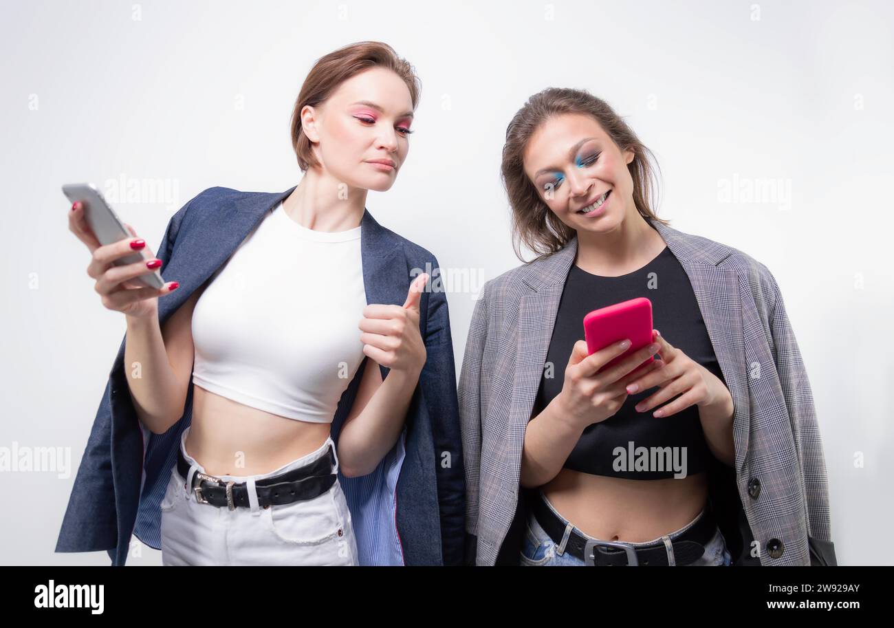 Zwei Freundinnen schreiben auf ihrem Smartphone und lachen. Blogger-Konzept. Tratsch. Gemischte Medien Stockfoto