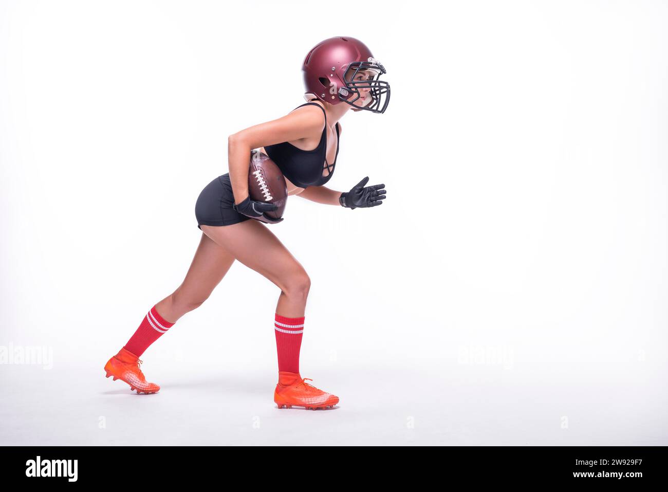 Eine Frau in der Uniform eines American Football-Mannschaftsspielers bereitet sich darauf vor, mit dem Ball zu laufen. Weißer Hintergrund. Sportkonzept. Gemischte Medien Stockfoto