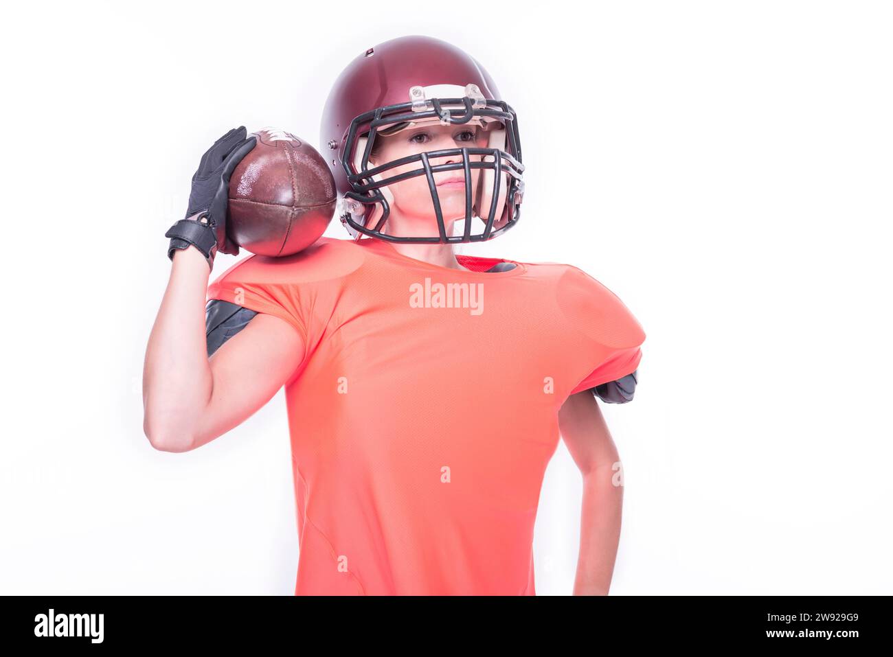 Frau in der Uniform eines American Football-Mannschaftsspielers, der mit einem Ball auf weißem Hintergrund posiert. Sportkonzept. Gemischte Medien Stockfoto