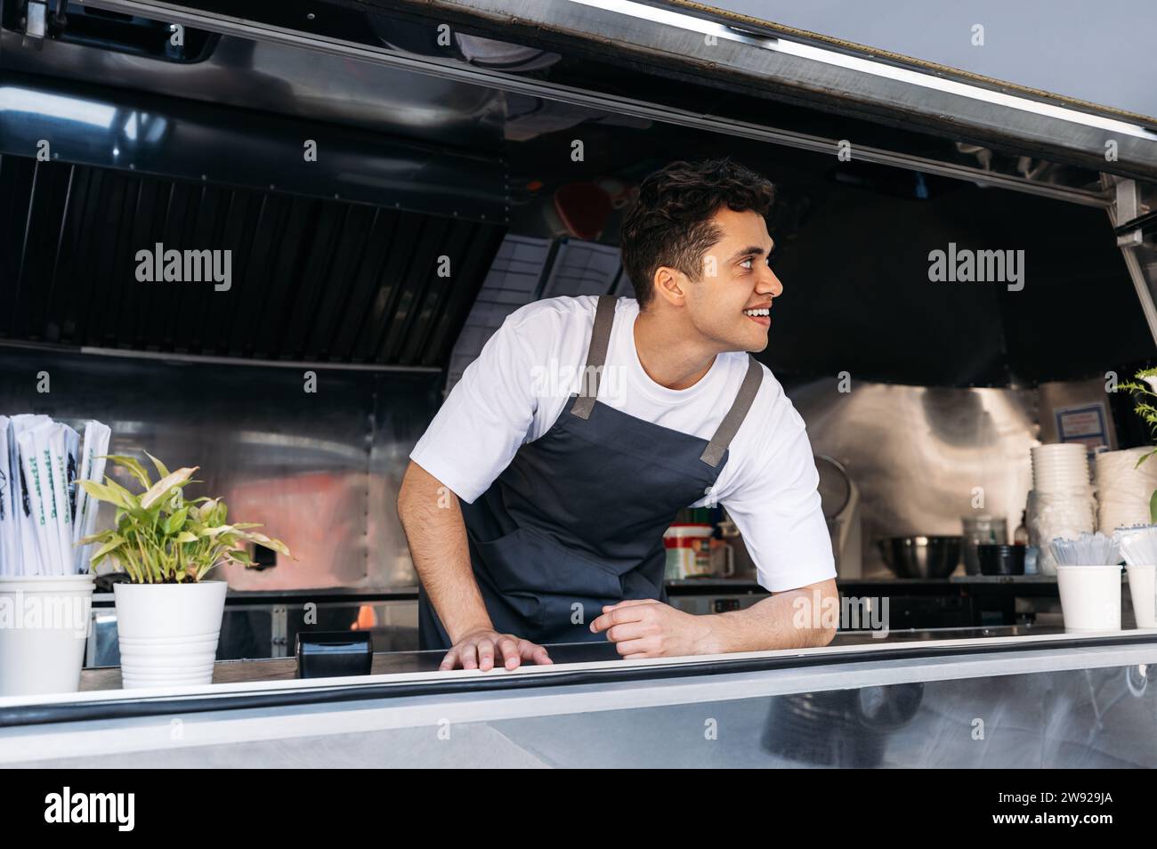 Zuversichtlicher Koch in der Essenskiste. Junger Besitzer von Food Trucks, der auf Kunden wartet. Stockfoto
