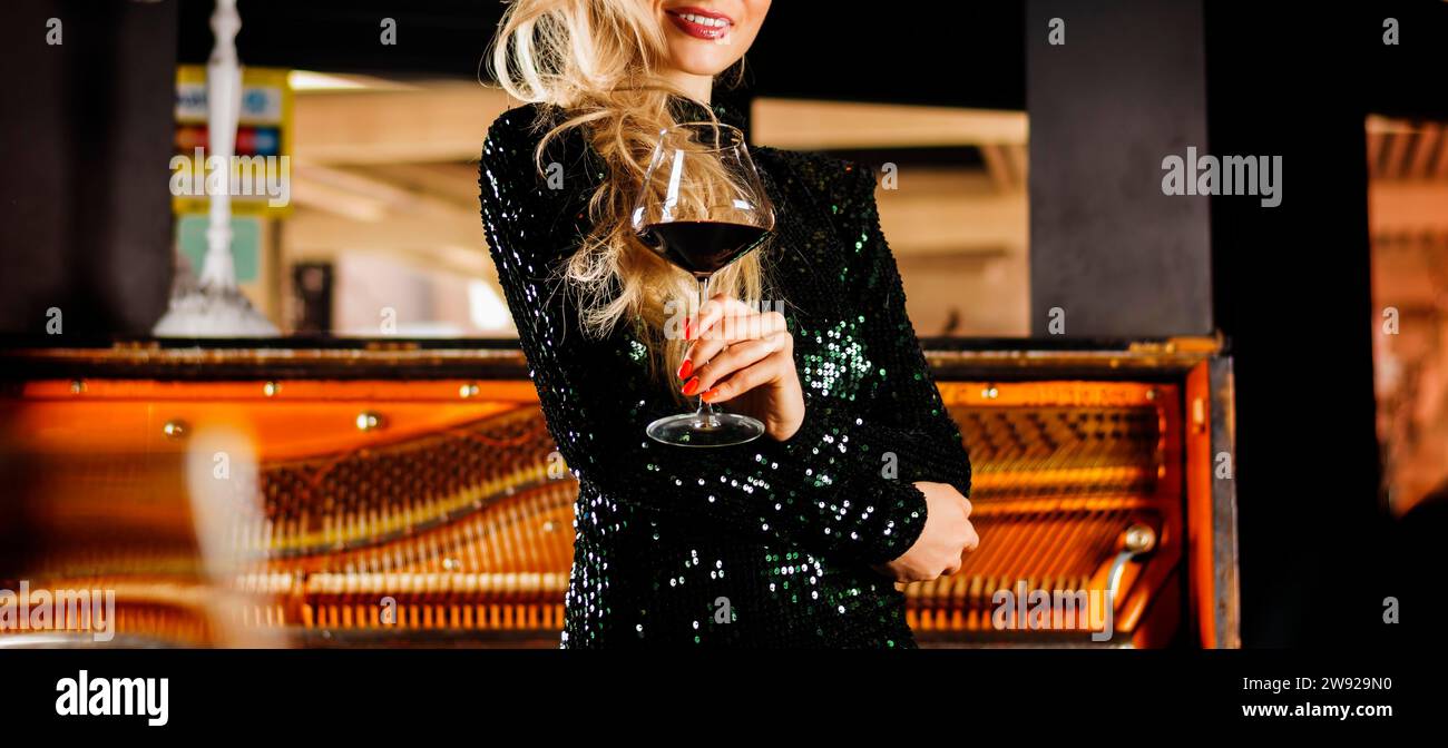 Das charmante Mädchen im Abendkleid genießt Musik und trinkt Rotwein. Gemischte Medien Stockfoto