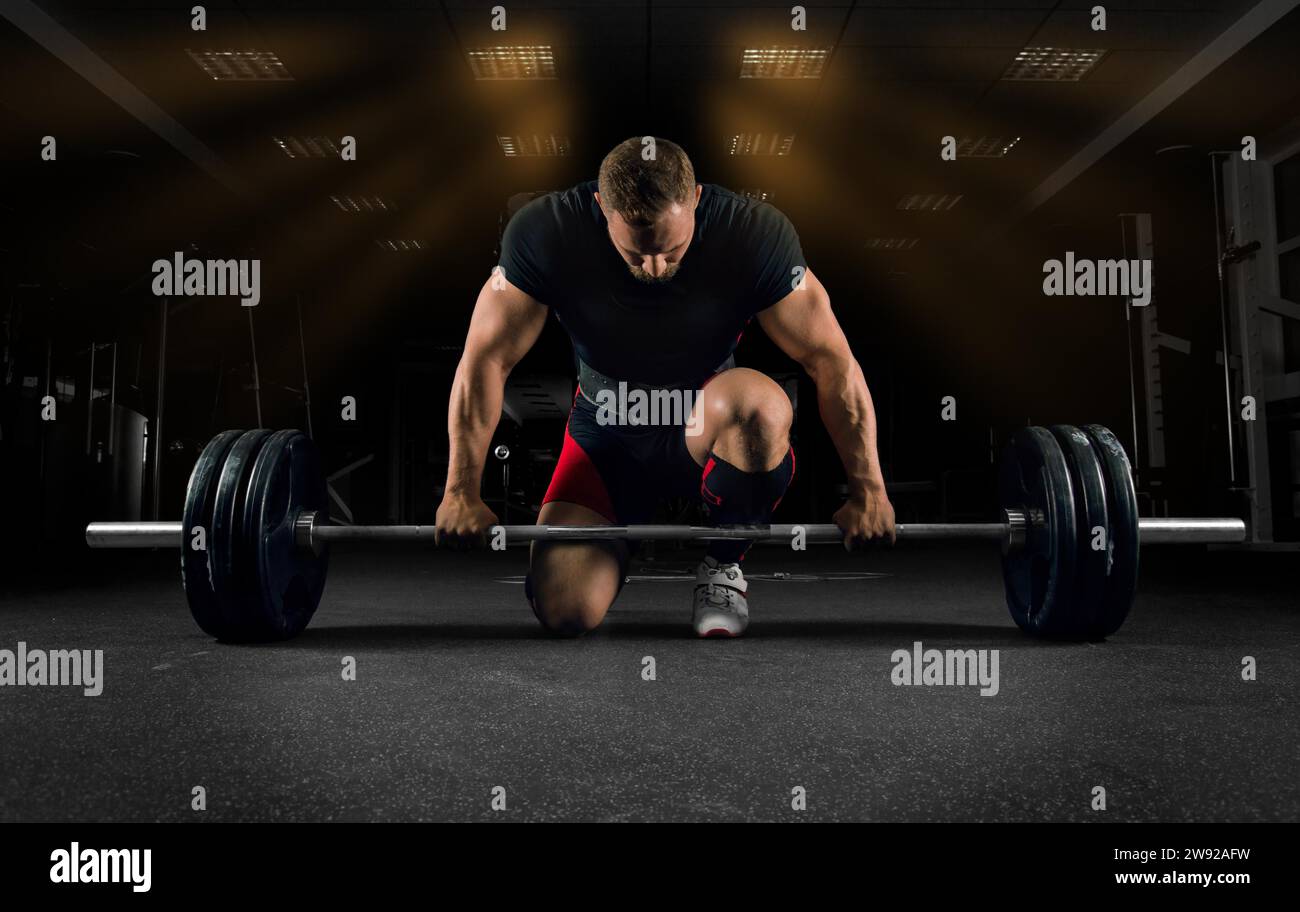 Der Athlet steht auf seinem Knie und in der Nähe der Bar im Fitnessstudio und bereitet sich auf einen Deadlift vor Stockfoto