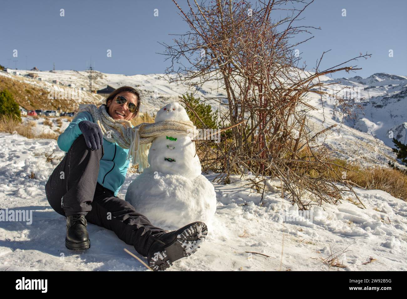Lateinische Frau, die auf gefrorenem Boden neben einem Schneemann sitzt Stockfoto