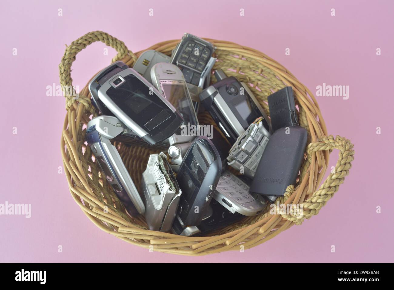 Ein Korb voller alter Handys auf rosa Hintergrund, Pokerkarten und Chips Stockfoto