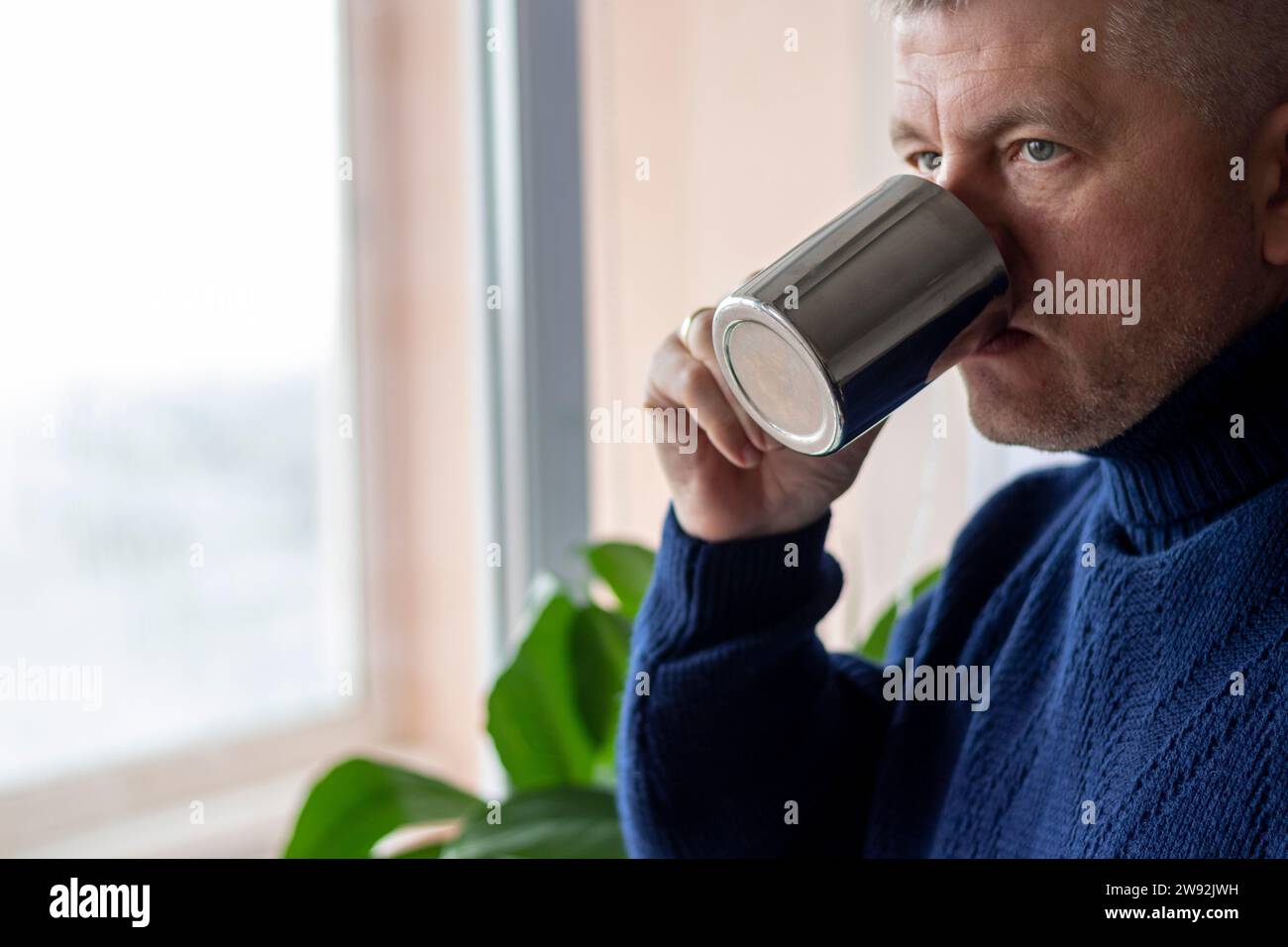 Porträt eines Mannes mittleren Alters mit grauen Haaren, der einen warmen, dunkelblauen Pullover trägt und Kaffee trinkt. Stockfoto