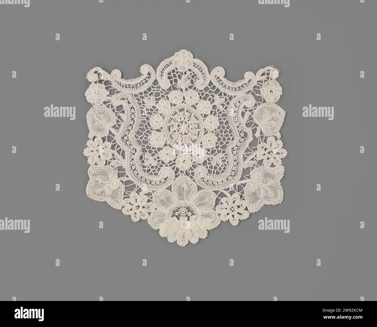 Slip of a Mixed Side, anonym, ca. 1900 Slip of a das of Natural-farbige Mixed Side - Spule in Kombination mit Nadelseite - Brussels Duchesse. In der Mitte eine Blume, die an zwei verschiedenen Rändern gefangen ist, mit einem Kranz aus elf Blüten, aus denen fünf Blattzweige hervorgehen. Bei einer groben Maas ist diese vollständig in fünf Voluten gefangen, die an den Seiten und am Boden von einem floralen Motiv umgeben sind. Die Motive sind mit Reliefkonturen versehen. Brüsseler Leinen (Material) Spitze gemischt / Brüssel gemischt Stockfoto