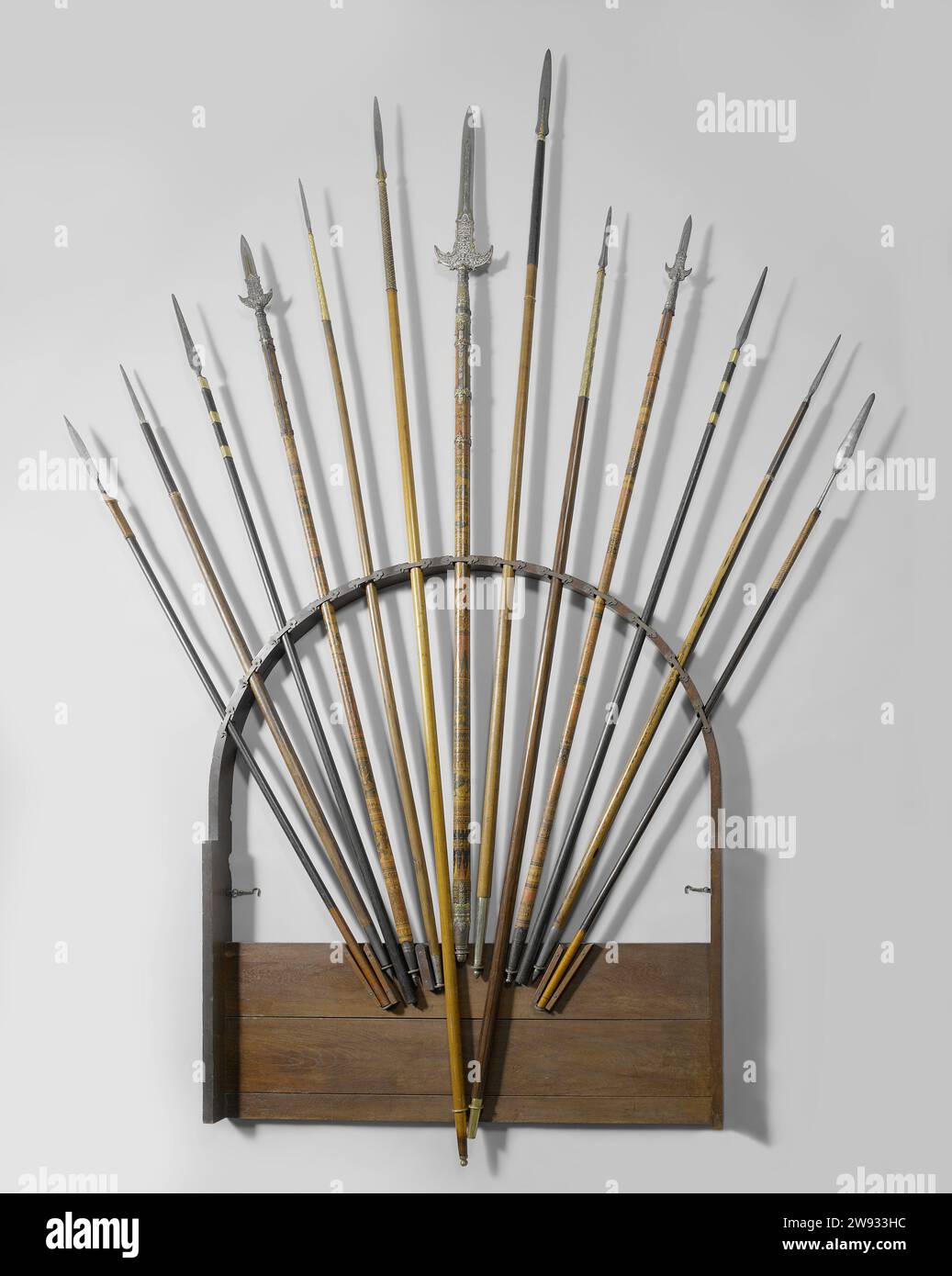 Speerregal von Generalgouverneur J. C. Baud, anonym, 1834 Holzbogen mit 13 ovalen Aussparungen für Stabwaffen. Jede Aussparung hat eine Messingklemme. Die Form der Klemme ist ein Rechteck mit einer Kleeblatt-drei-Form an beiden Enden. Die Rückwand von Boog besteht aus zwei breiten Dielen und einem schmalen Brett, das mit Stift und Loch in den Bogen passt. Fünf Leisten und elf Kupferringe auf der oberen Ablage der Rückwand zur Führung der Lanzen im Rack. Indonesien Teakholz (Holz). Schneiden/Guss aus Messing (Legierung) Stockfoto