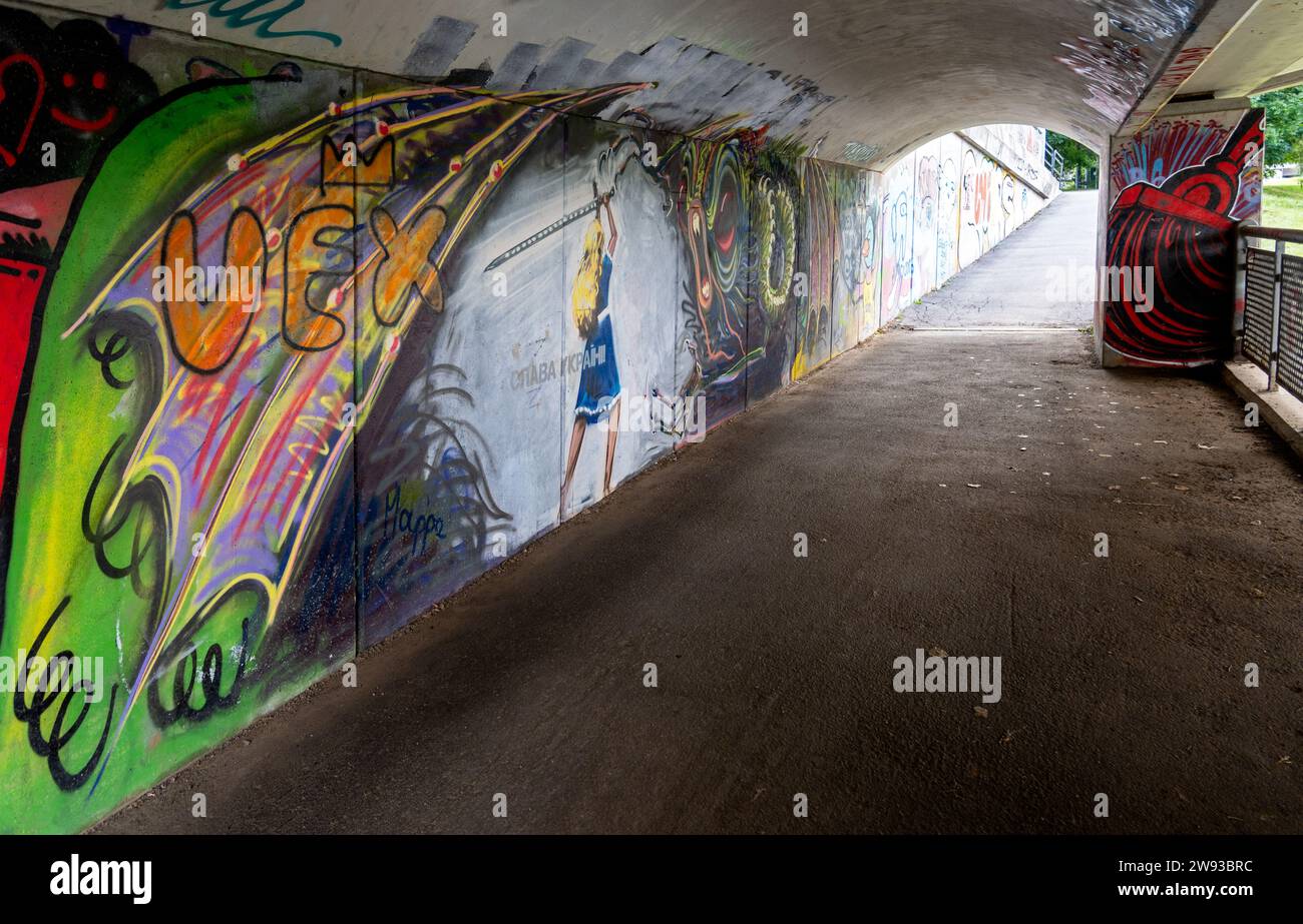 Mädchen in blauem Kleid mit Schwert greift ein Monster an: Graffiti unter der Kroonuaia-Brücke, Tartu, Estland Stockfoto