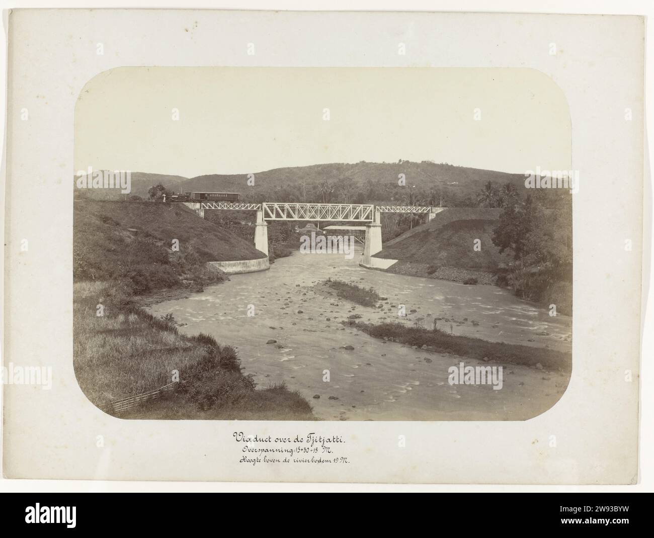 Viadukt über dem Tjitjatti. Spannweite: 15 + 30 + 15 M. Höhe über dem Flussboden 19 M., Anonym, 1880 - 1888 Fotografieren Sie das Viadukt oder die Eisenbahnbrücke über dem Tjitjatti. Der Zug wartet links von der Brücke. Teil einer Gruppe von 62 Fotos in einer Box mit der Aufschrift „Staatsspoorwegen auf Java“ von 1888. Java Photographic Support Albumendruck Java Stockfoto