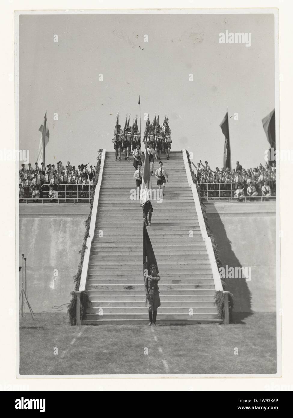 Jugendsturm im Stadion Galgenwaard, 1942 Foto Eine lange Reihe von Mitgliedern des Jeugdstorm kommt am 20. Juni 1942 im Stadion Galgenwaard in Utrecht herunter. Im Stadion werden sie den 3000 vereidigten Führungskräften des NSB beiwohnen, unten auf der Treppe steht ein Wehrmachtssoldat mit einer Flagge. Es gibt Mitglieder des Jugendsturms auf den Tribünen, links und rechts der Treppe. Ein Teil bringt den NSB-Gruß: Gestreckter Arm wie der Hitler-Gruß und Ruf: Houzee. Die Eidesfeier war das Ergebnis eines Kompromisses zwischen den Deutschen und der NSB, die Deutschen wollten keinen Eid o Stockfoto