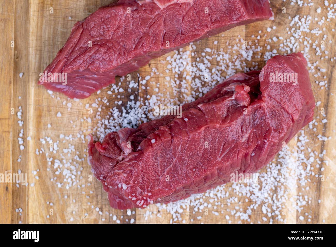 Geschnittenes Stück frisches rohes Rindfleisch beim Salzen, Zubereitung von Halbfertigprodukten mit Rindfleisch mit Salz Stockfoto