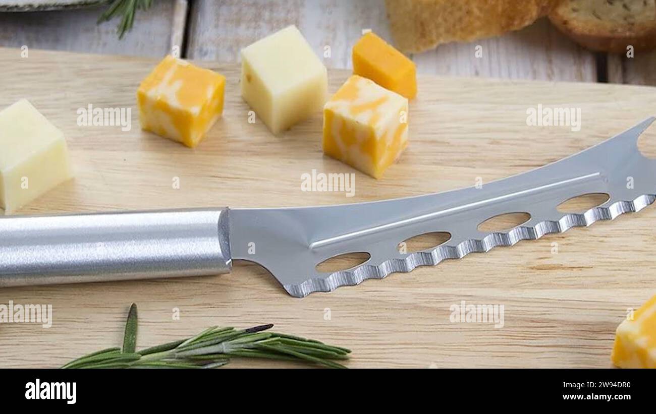 Schneiden von Weichkäse mit einem speziellen Käsemesser aus Edelstahl. Seine Klinge, die mit Löchern verziert ist, schafft perfekte Käsescheiben. Küchenausstattung Stockfoto