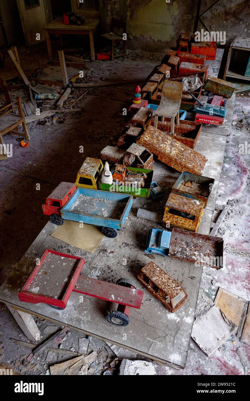 Verlassener Raum mit verfallenen Wänden und Boden, gefüllt mit staubbedeckten Vintage-Spielzeugwagen. Stockfoto