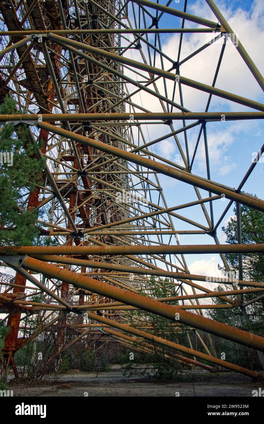 Das Foto zeigt eine aufwändige Metallkonstruktion inmitten karger Vegetation unter einem wolkenblauen Himmel. Duga ist eine sowjetische Radarstation über dem Horizont Stockfoto