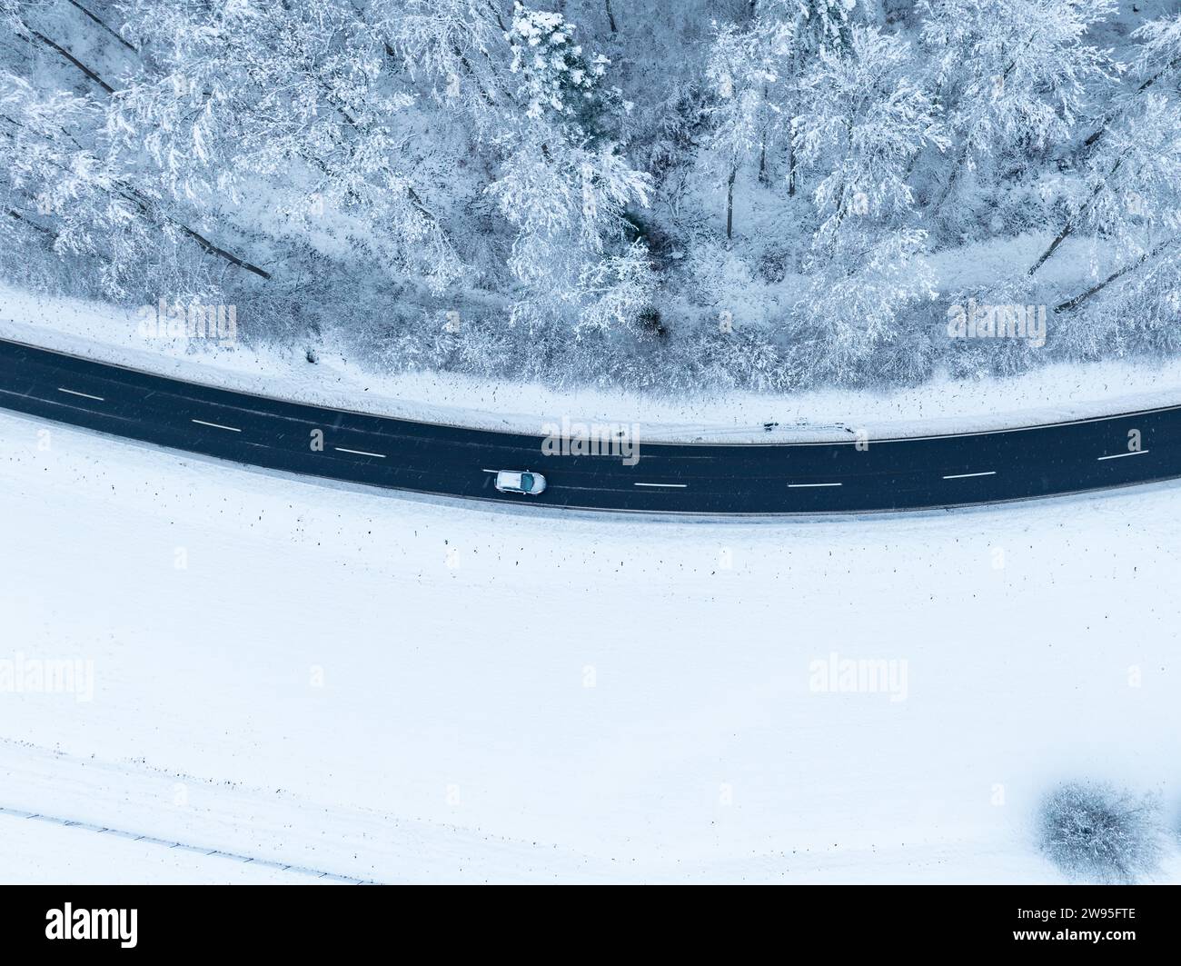 Ein einzelnes Fahrzeug, das auf einer verschneiten Straße aus der Luft fährt, Gechingen, Luftaufnahme, Schwarzwald, Deutschland Stockfoto