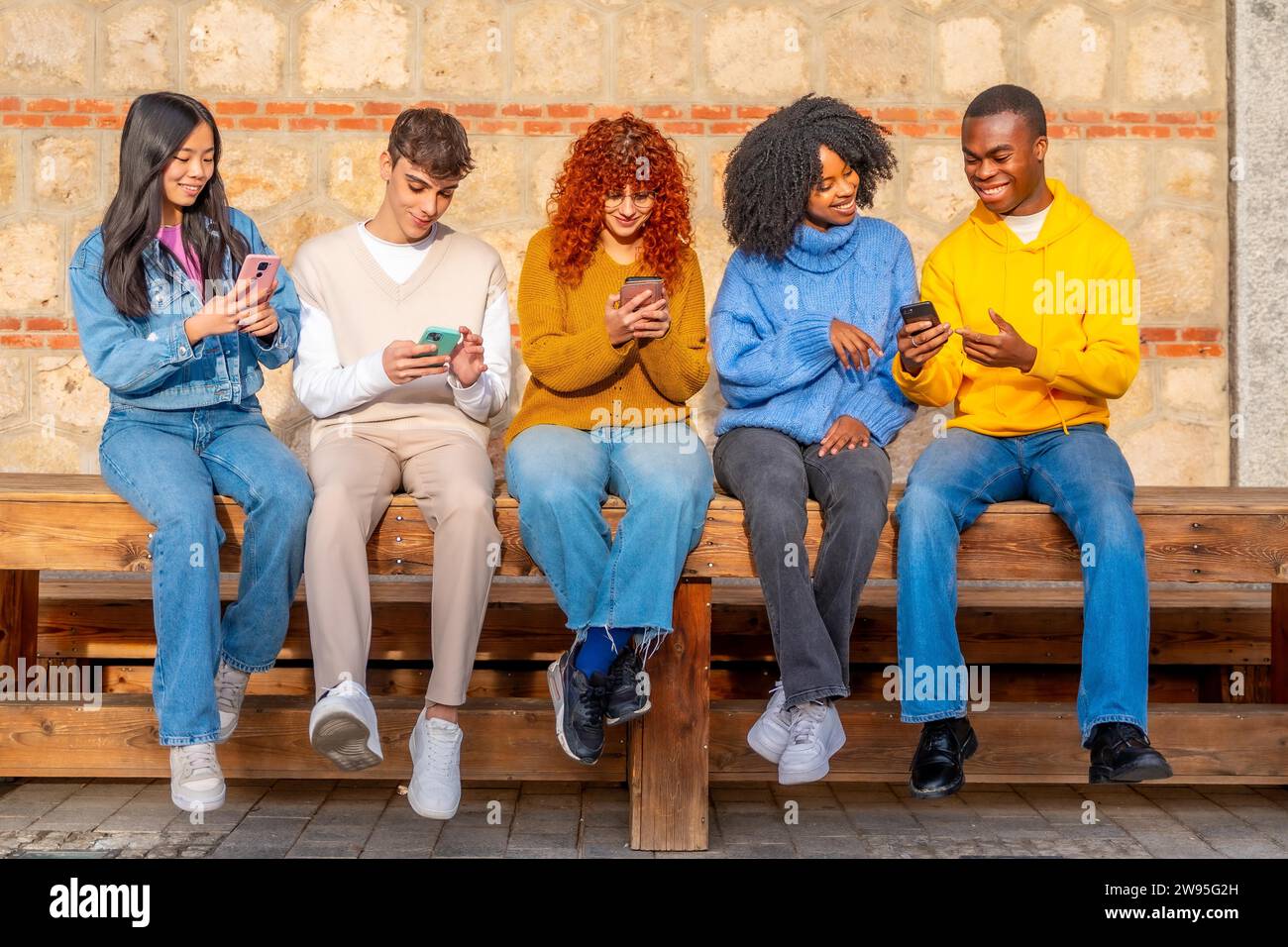 Frontalansicht einer Gruppe multiethnischer junger Freunde, die auf einer Bank in der Stadt sitzen Stockfoto