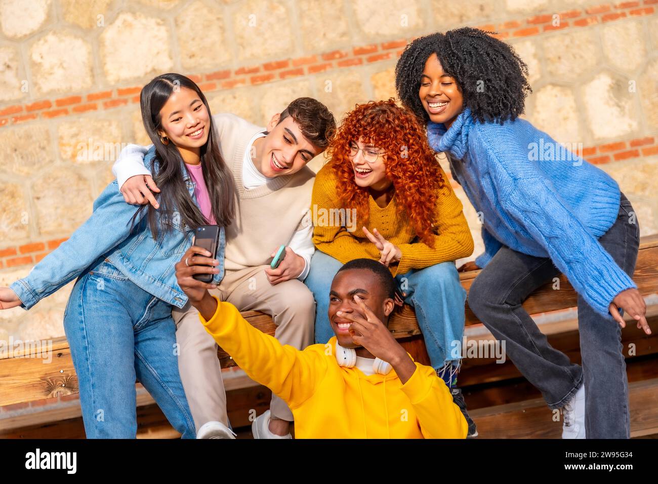 Coole Gruppe von Teenagern, die gemeinsam ein Selfie machen und draußen auf einer Holzbank sitzen Stockfoto