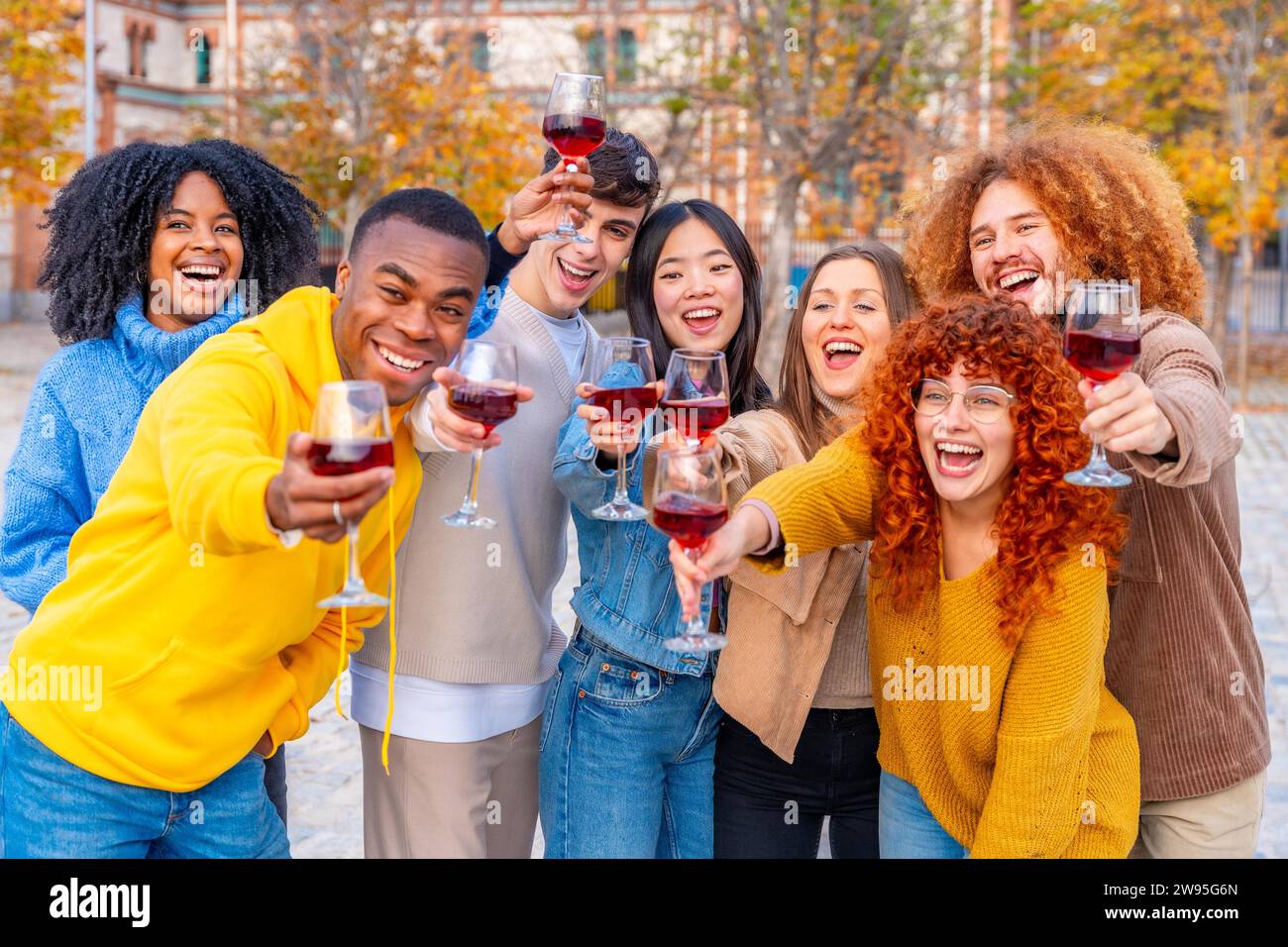 Multiethnische Jugendliche lächeln und tosten mit Wein vor die Kamera auf der Straße Stockfoto