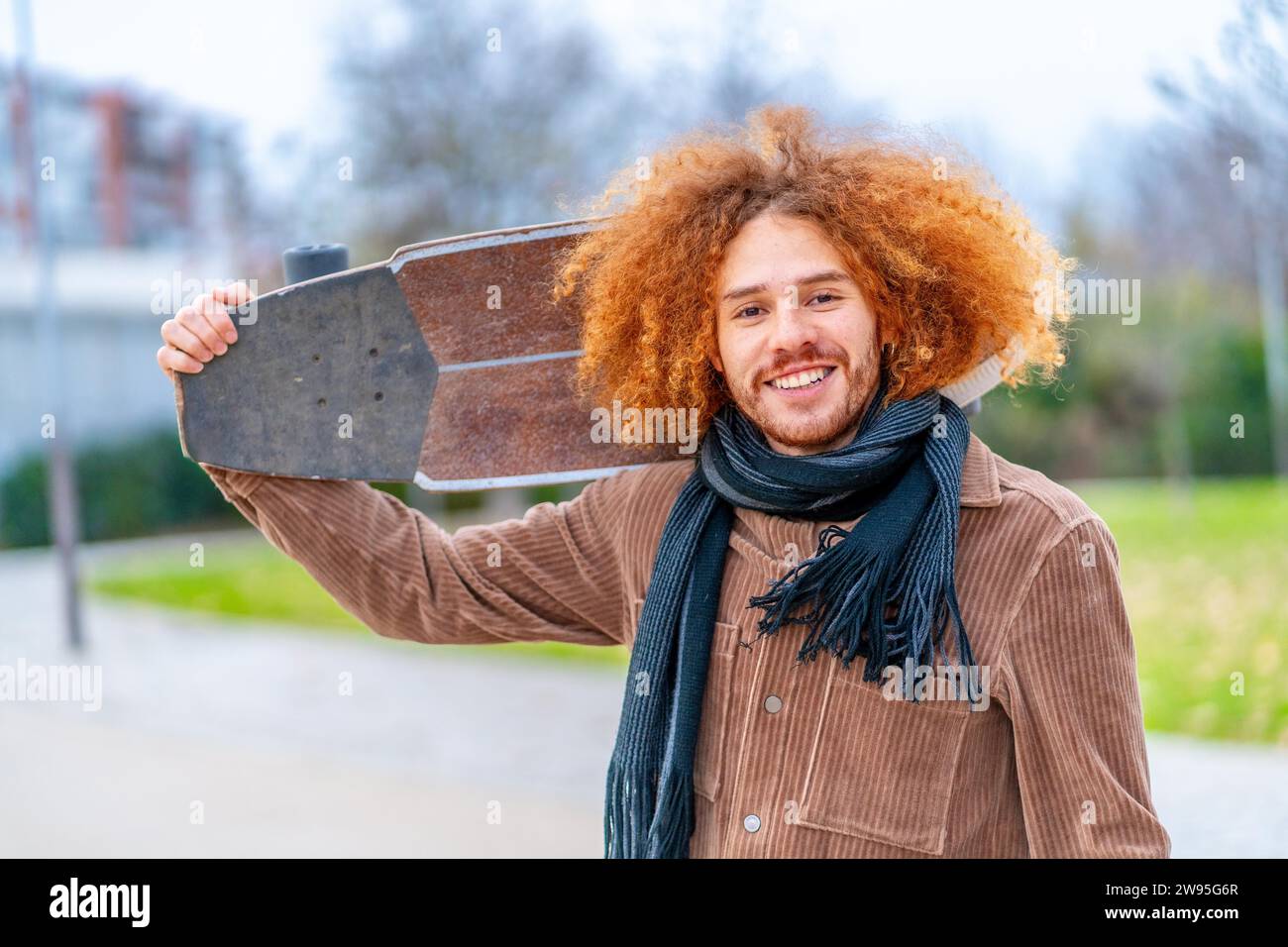 Porträt eines rothaarigen Skaters, der in einem Stadtpark einen Schlittschuh trägt und in die Kamera lächelt Stockfoto