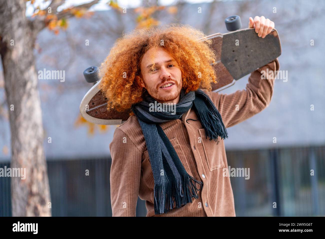 Cooler Mann mit lockigen rothaarigen Haaren, der ein Skateboard in der Stadt trägt Stockfoto
