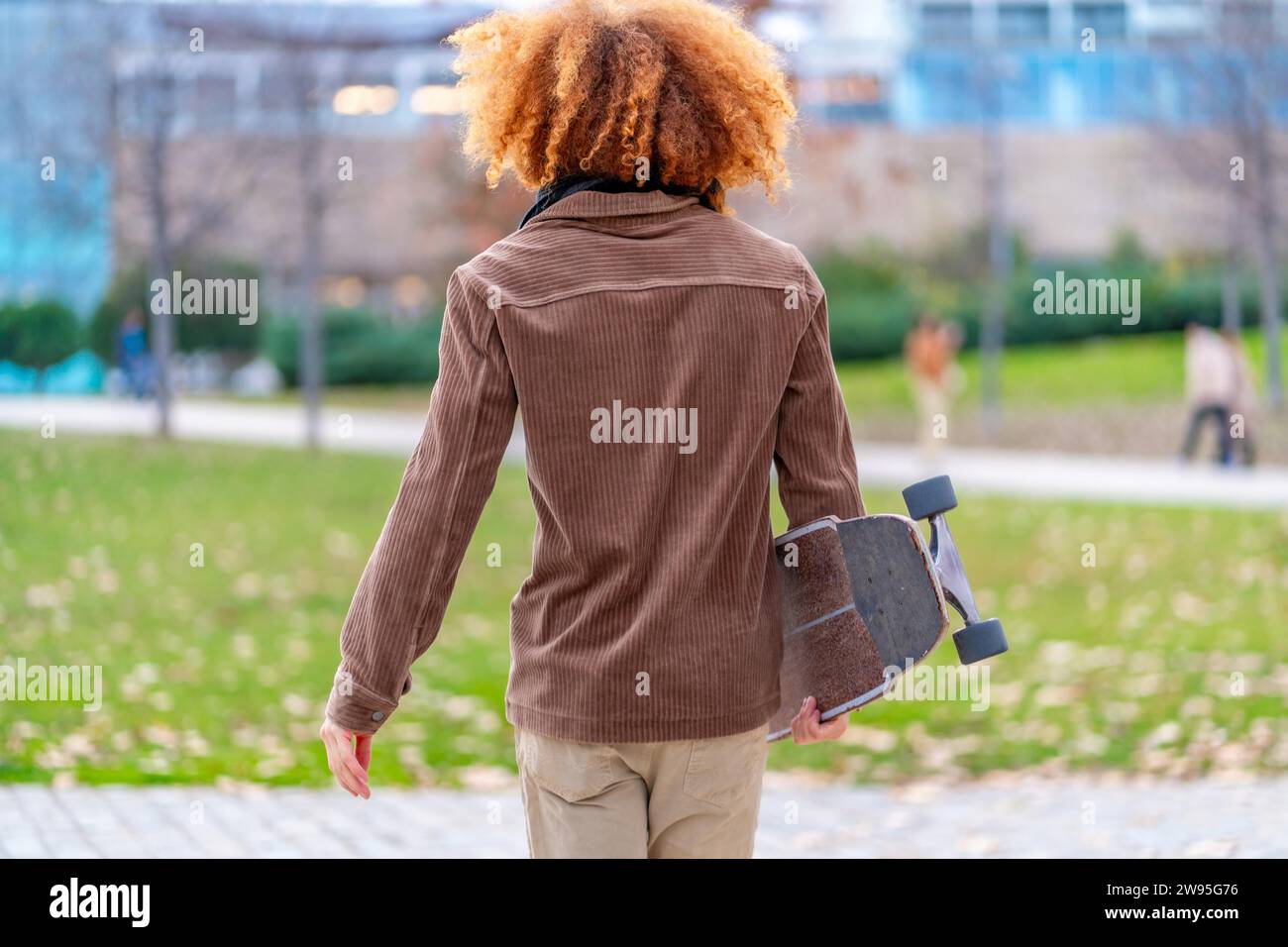 Rückansicht eines Mannes, der ein Skateboard in einem Park trägt Stockfoto