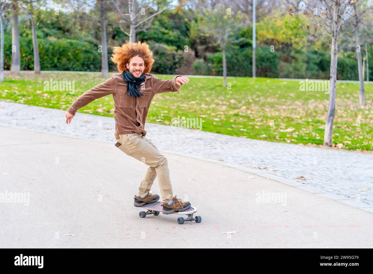 Rothaarige Lockenhaare junger Mann, der im Herbst in einem Park Schlittschuhlaufen will Stockfoto